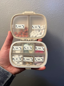 Reviewer holding their pill organizer filled with pills and with the compartments labeled 