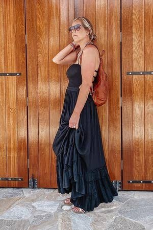 a reviewer in a layered black dress and sunglasses posing against a wooden door