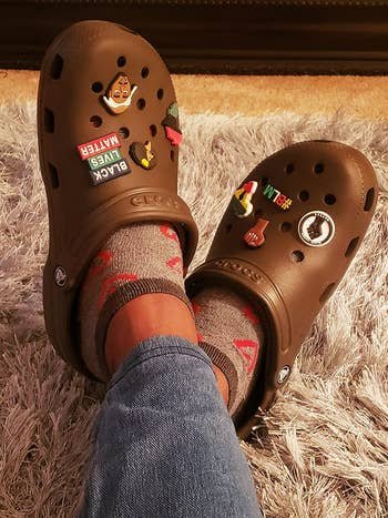 Person wearing gray socks and brown Crocs adorned with various colorful charms