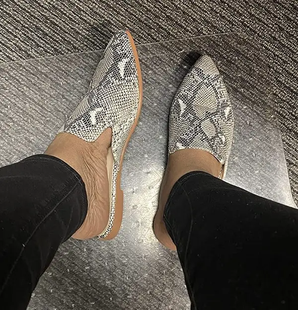 Feet wearing a pair of snake skin mules