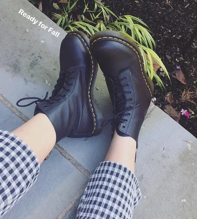 a reviewer photo of the black dr. martens worn with checkered pants. Text reads 