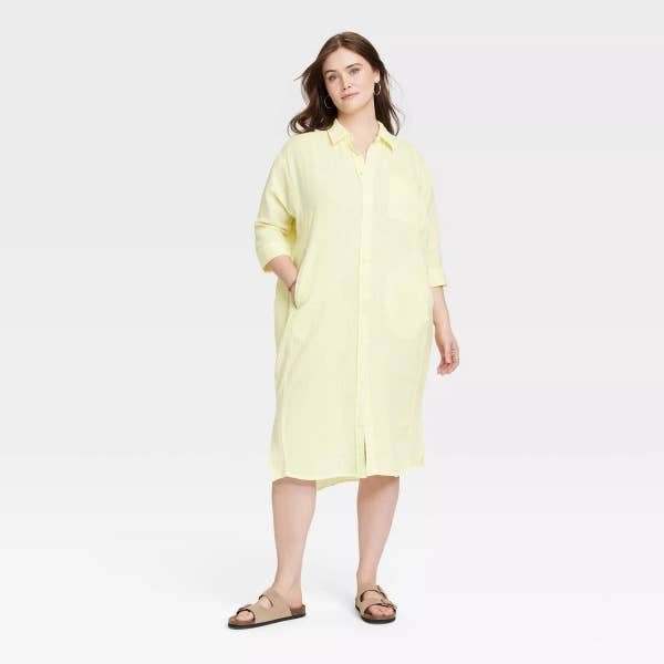 Model standing in a light yellow mid-length shirt dress with buttons and collar, paired with brown sandals